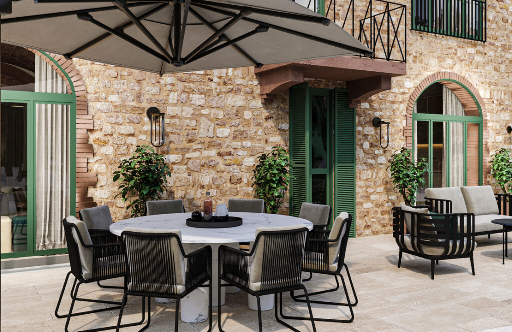 Outdoor dining area with a round table and modern chairs under a large umbrella, surrounded by stone walls and green shutters, featuring potted plants for a cozy ambiance. | Only on SopranoVillas
