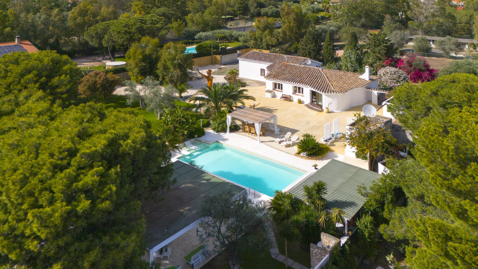 Aerial view of a beautiful villa featuring a sparkling swimming pool, surrounded by lush greenery and colorful flowers, with a spacious outdoor area for relaxation and entertainment. | Only on SopranoVillas