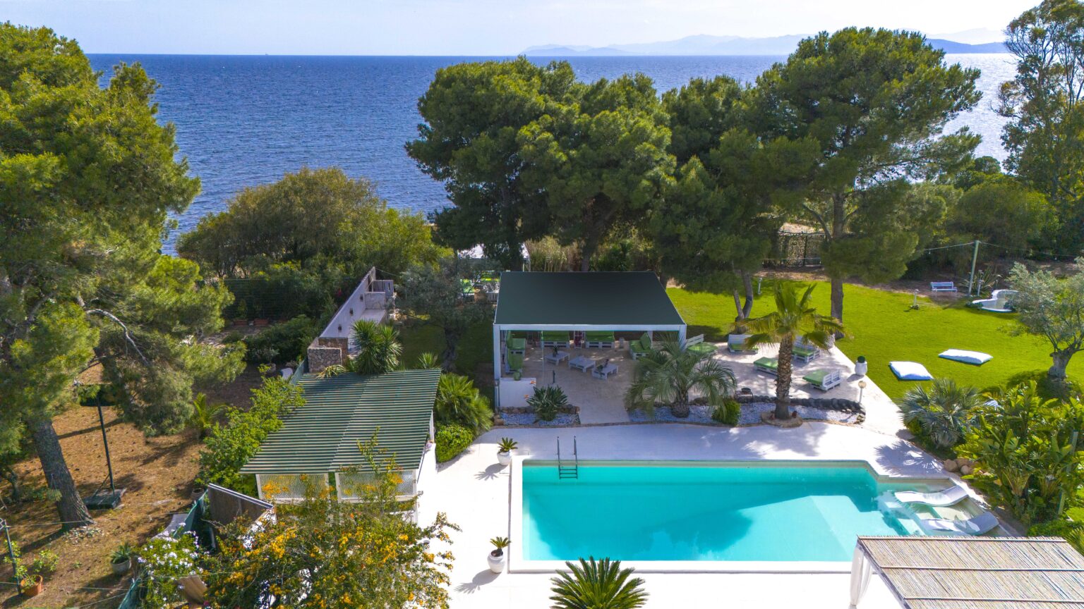 Aerial view of a luxurious villa with a swimming pool surrounded by lush greenery and overlooking the ocean, ideal for a relaxing getaway. | Only on SopranoVillas