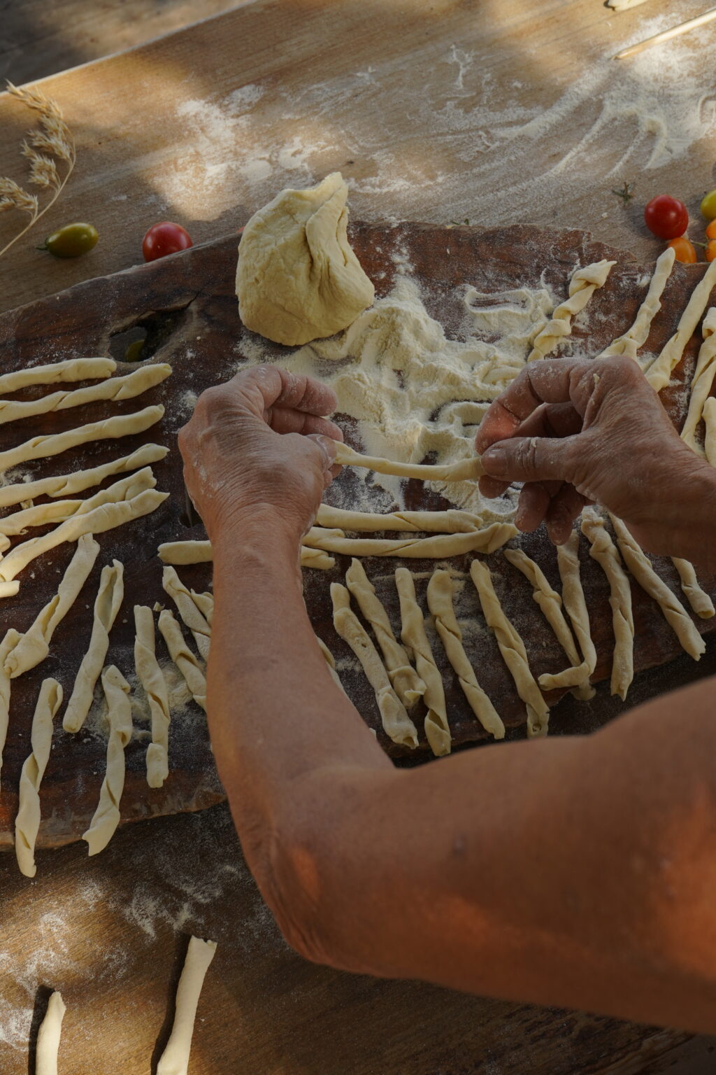 Hands shaping fresh pasta on a wooden surface, surrounded by strips of dough ready for cooking. | Only on SopranoVillas
