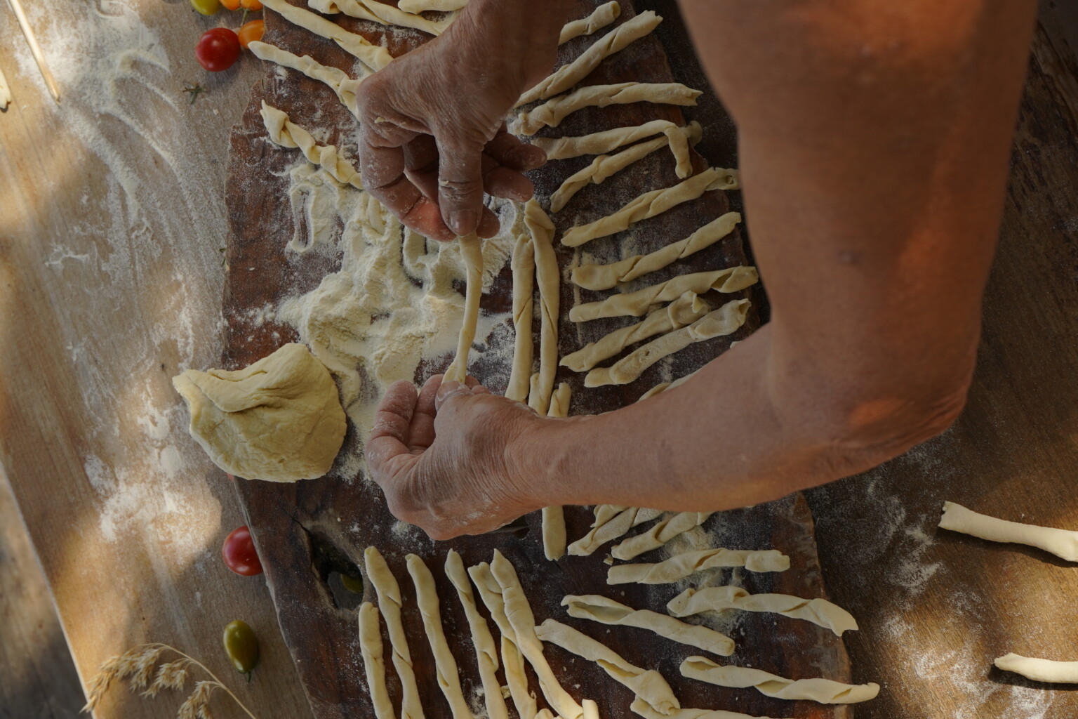 Hands shaping fresh pasta on a wooden surface, surrounded by strips of dough ready for cooking. | Only on SopranoVillas