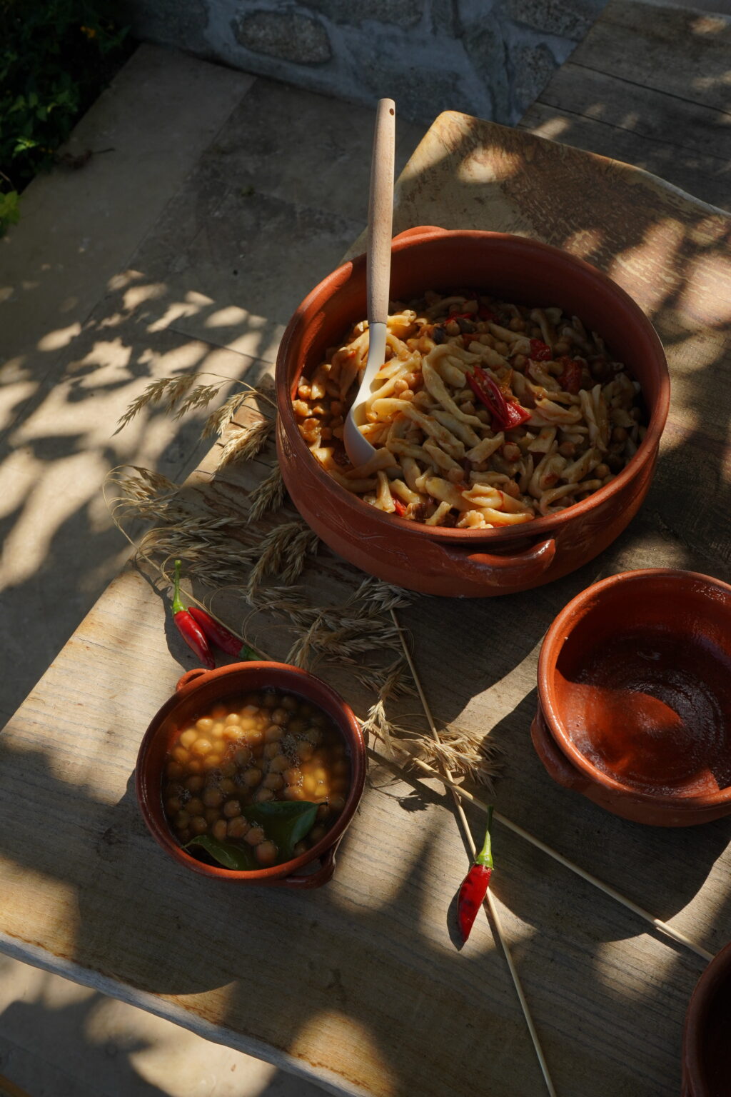 Traditional clay pots filled with pasta and spices, with a side of lentil dish, set on a rustic wooden table surrounded by dried herbs. | Only on SopranoVillas