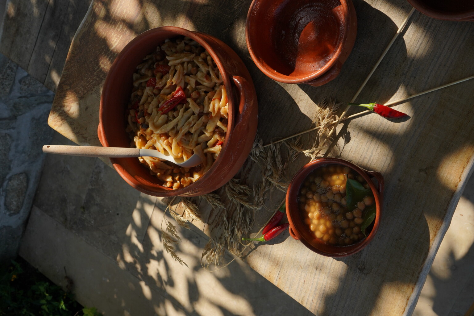 Traditional clay pots filled with pasta and spices, with a side of lentil dish, set on a rustic wooden table surrounded by dried herbs. | Only on SopranoVillas
