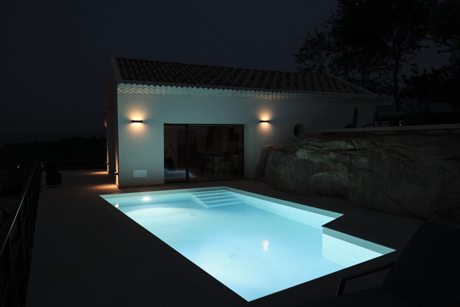Modern villa at night featuring a illuminated swimming pool and exterior lighting, surrounded by natural stone elements. | Only on SopranoVillas