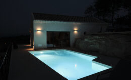 Modern villa at night featuring a illuminated swimming pool and exterior lighting, surrounded by natural stone elements.