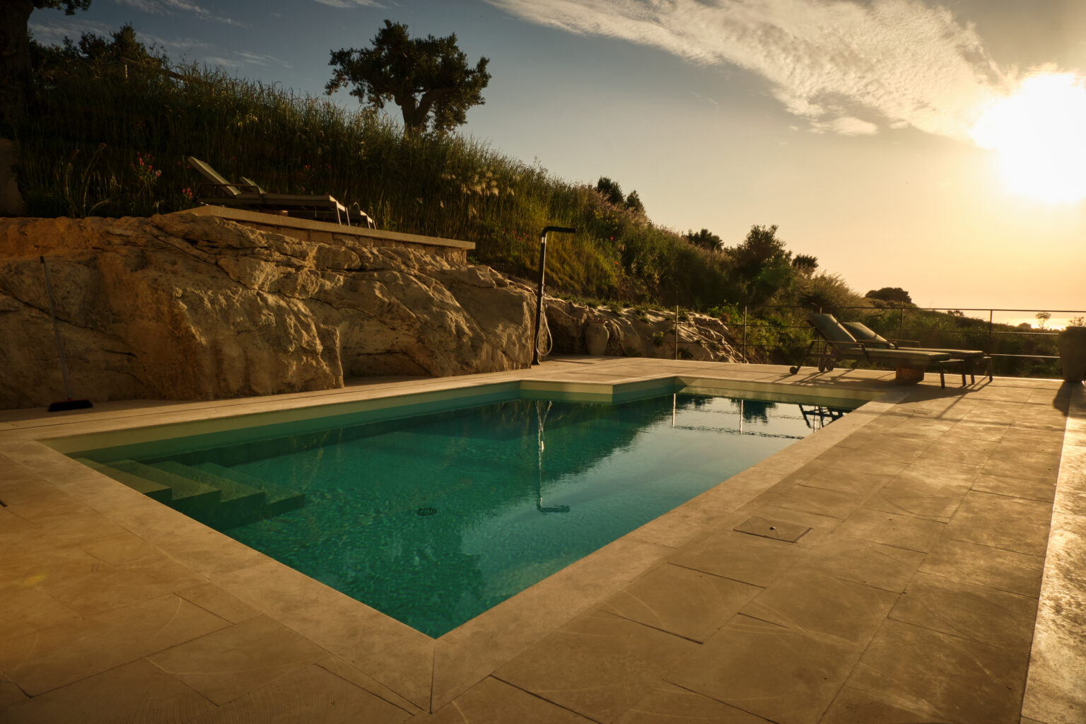 Serene outdoor swimming pool surrounded by natural stone and greenery, with a sunset casting warm light over the scene. Ideal for relaxation and leisure in a tranquil setting. | Only on SopranoVillas