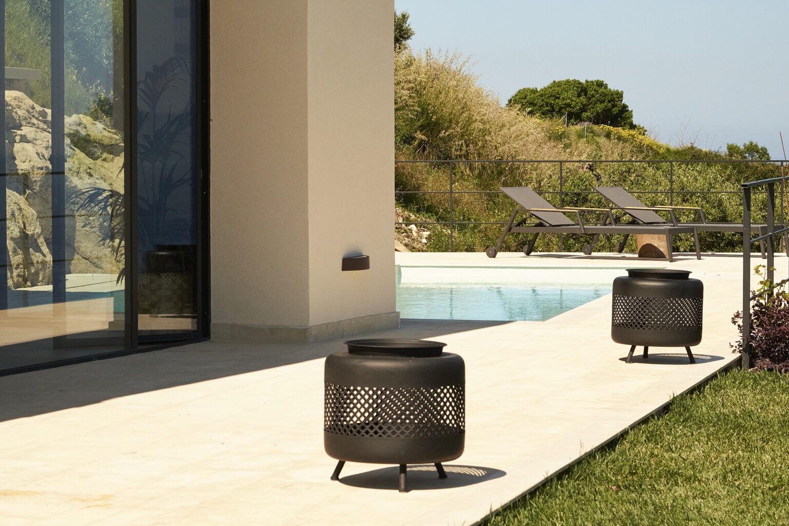 Outdoor patio featuring modern metal fire pits beside a swimming pool, with lounge chairs and lush greenery in the background. | Only on SopranoVillas