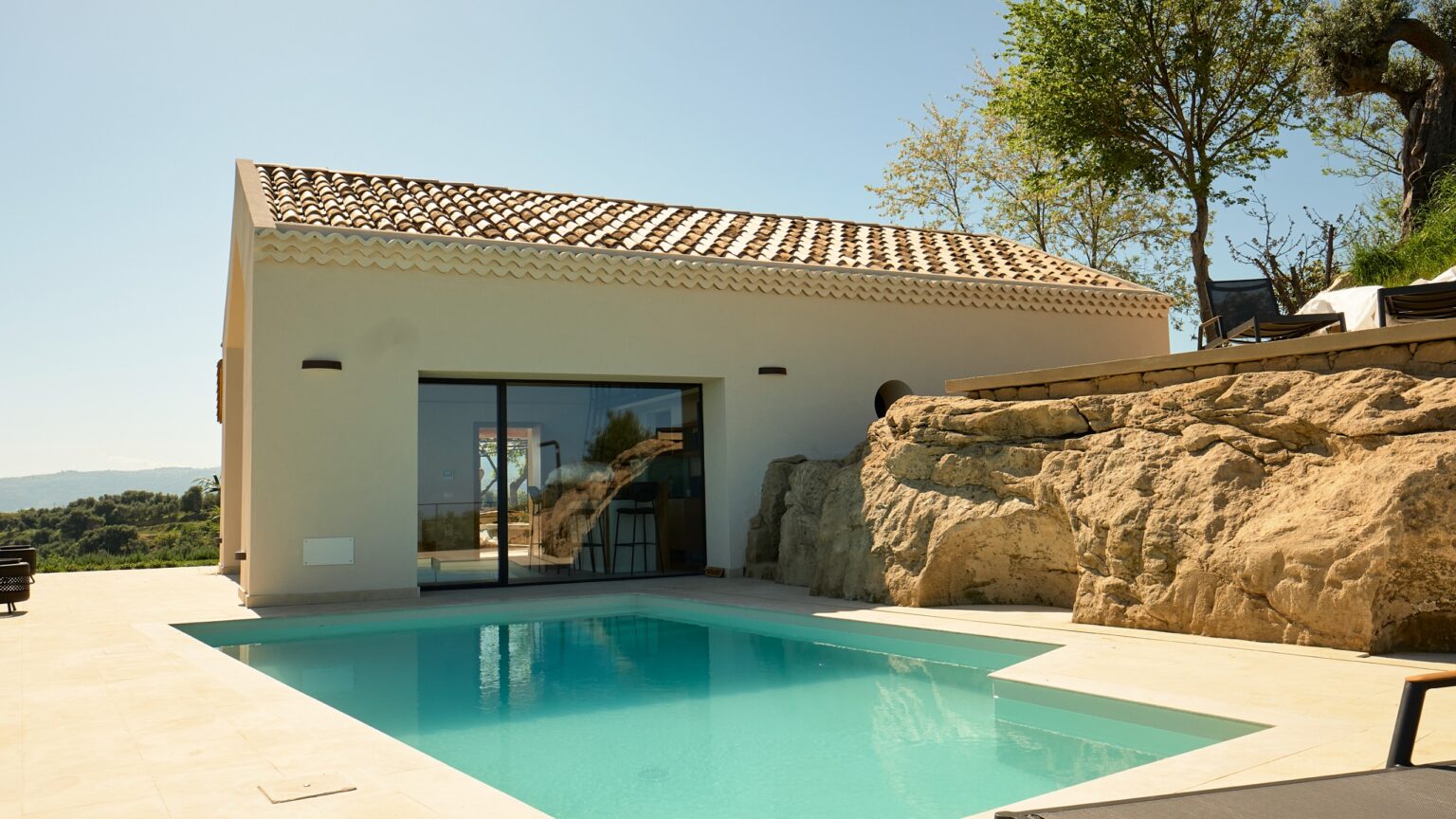 Modern villa with a private swimming pool, featuring a minimalist design and natural stone accents, surrounded by lush greenery and scenic views. Ideal for luxury retreats and vacation getaways. | Only on SopranoVillas