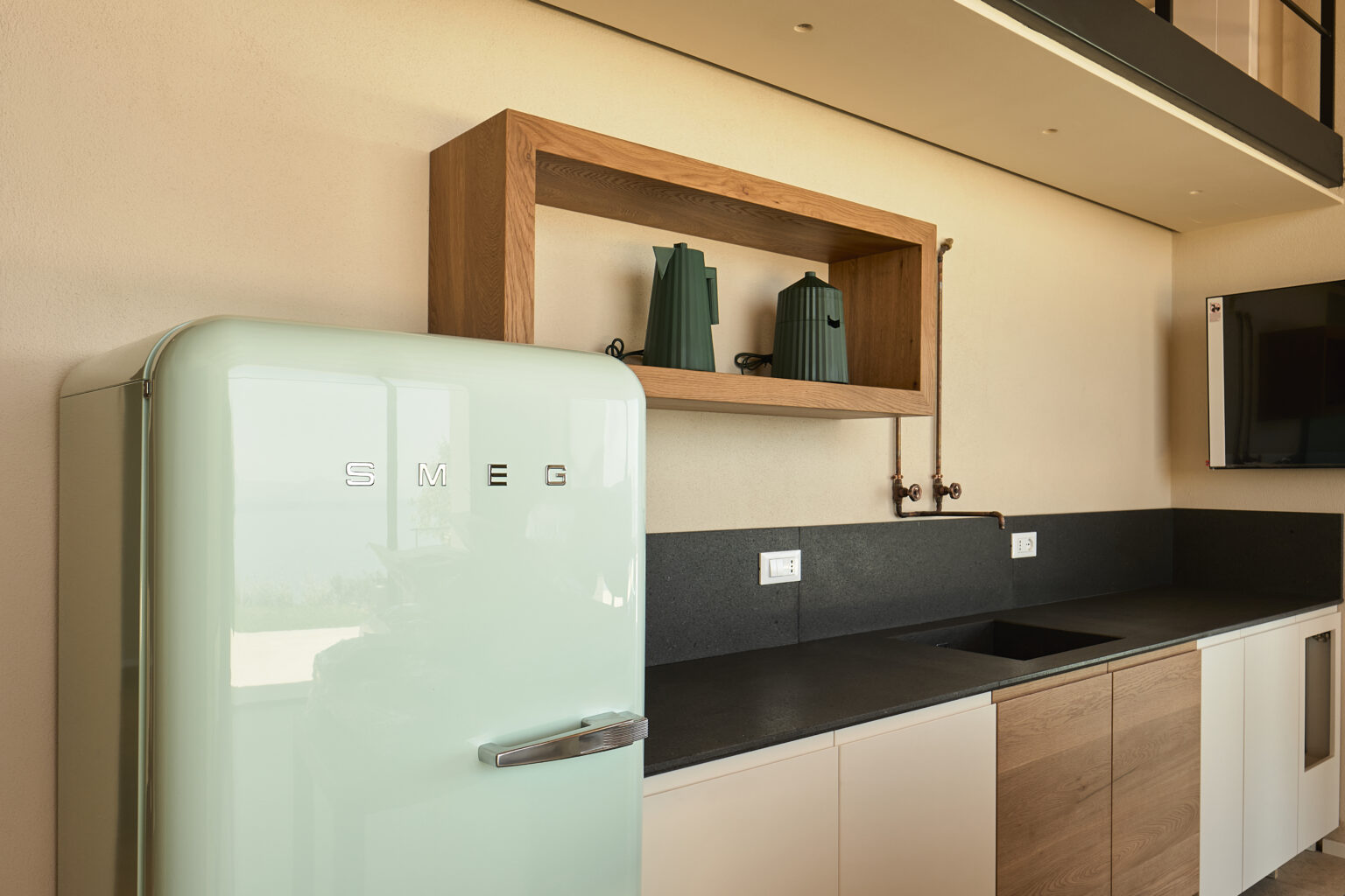 Retro mint green refrigerator in a modern kitchen with wooden shelves displaying decorative items, complemented by a sleek black countertop and cabinetry. | Only on SopranoVillas