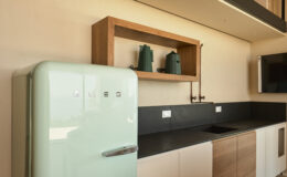 Retro mint green refrigerator in a modern kitchen with wooden shelves displaying decorative items, complemented by a sleek black countertop and cabinetry.