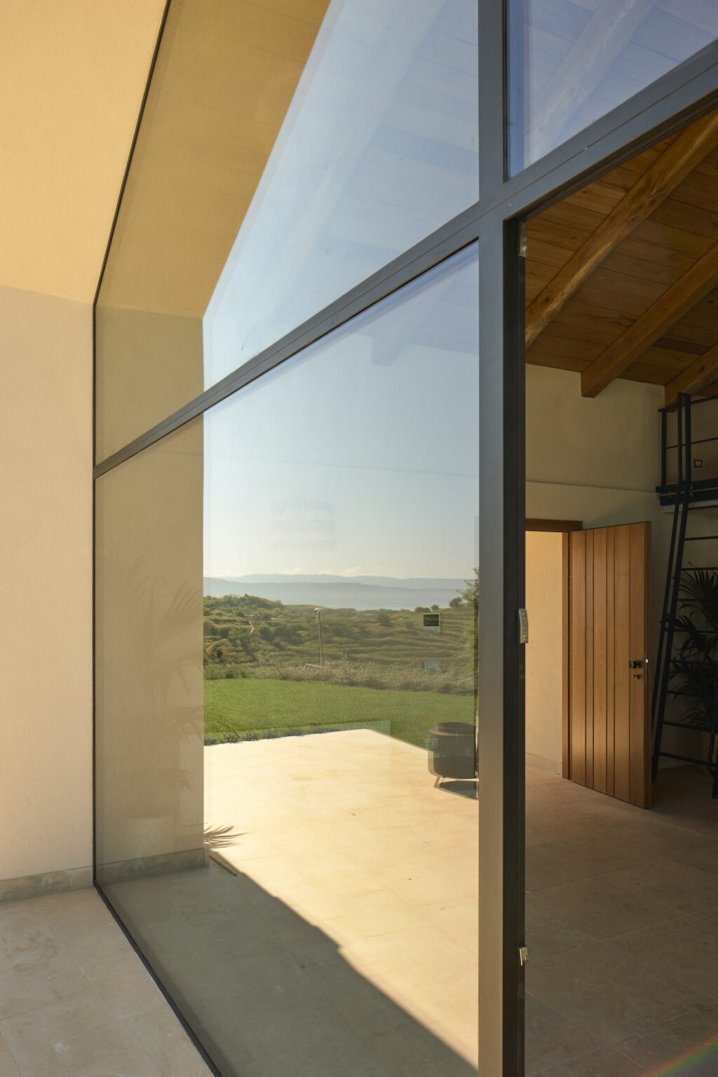 Modern glass door reflecting a scenic view of rolling hills and distant mountains, showcasing a blend of indoor and outdoor living spaces. | Only on SopranoVillas