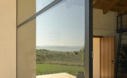 Modern glass door reflecting a scenic view of rolling hills and distant mountains, showcasing a blend of indoor and outdoor living spaces.