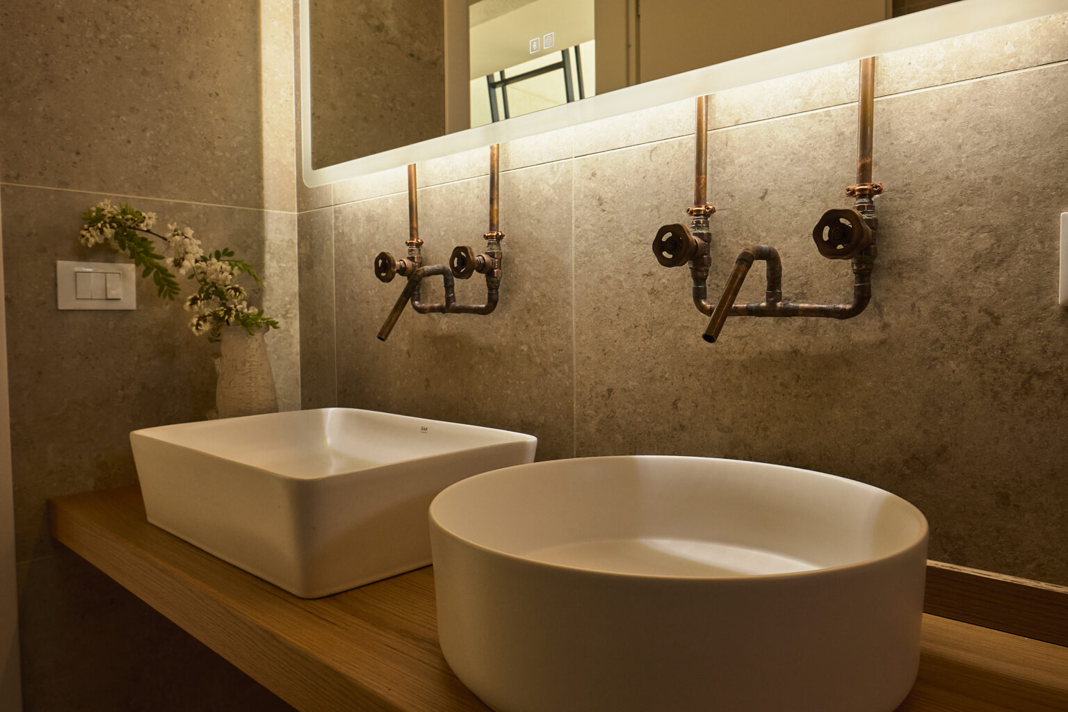 Modern bathroom design featuring two stylish vessel sinks on a wooden countertop, with industrial-style faucets and ambient lighting, creating a warm and inviting atmosphere. | Only on SopranoVillas