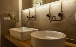 Modern bathroom design featuring two stylish vessel sinks on a wooden countertop, with industrial-style faucets and ambient lighting, creating a warm and inviting atmosphere.