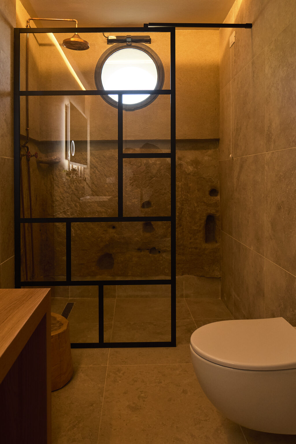 Modern shower enclosure with black metal frame and textured stone walls, featuring a minimalist design and wooden bench for added comfort. | Only on SopranoVillas