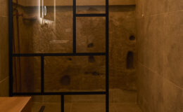 Modern shower enclosure with black metal frame and textured stone walls, featuring a minimalist design and wooden bench for added comfort.