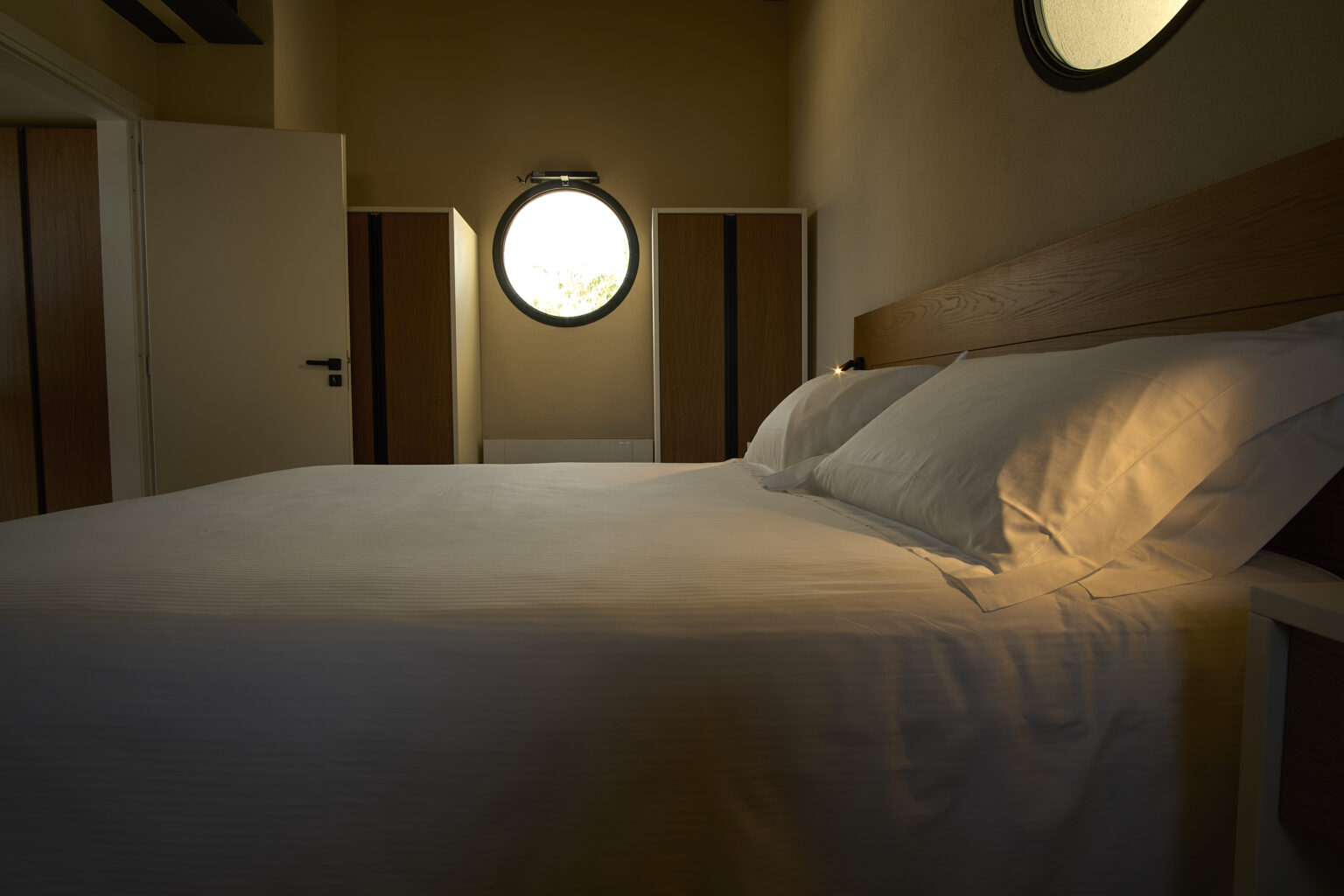 Cozy bedroom interior featuring a neatly made bed with white linens, soft lighting, and round windows, creating a warm and inviting atmosphere. | Only on SopranoVillas