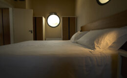 Cozy bedroom interior featuring a neatly made bed with white linens, soft lighting, and round windows, creating a warm and inviting atmosphere.