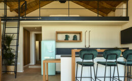Modern kitchen interior featuring a loft design, with a green retro refrigerator, stylish bar stools, and a sleek countertop. The space is illuminated by natural light, showcasing wooden beams and contemporary decor elements.