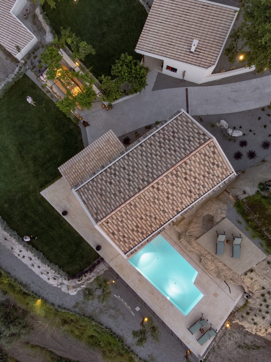 Aerial view of a modern house with a tiled roof, surrounded by a landscaped yard and a swimming pool, showcasing outdoor seating areas and greenery. | Only on SopranoVillas