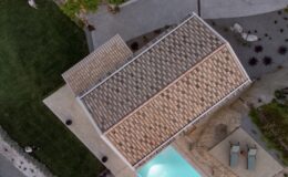 Aerial view of a modern house with a tiled roof, surrounded by a landscaped yard and a swimming pool, showcasing outdoor seating areas and greenery.