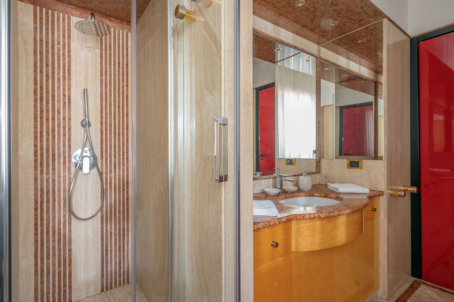 Modern bathroom featuring a glass shower, elegant marble countertop, and stylish red accents, designed for comfort and functionality. | Only on SopranoVillas