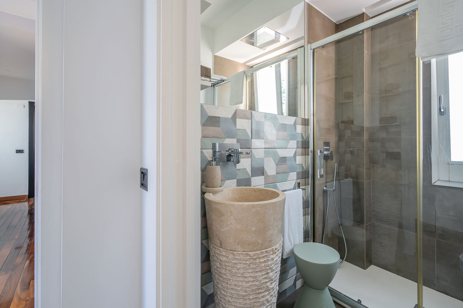 Modern bathroom featuring a walk-in shower with glass doors, stylish tiled walls in neutral tones, a unique stone basin, and a minimalist toilet, creating a sleek and functional space. | Only on SopranoVillas
