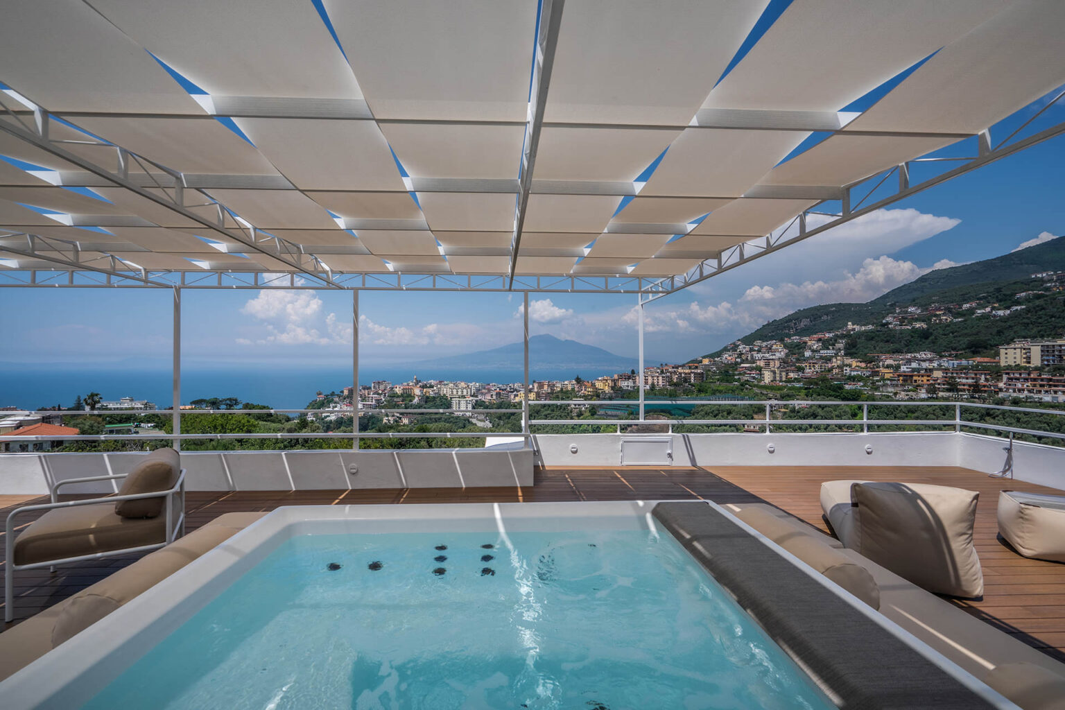 Luxury rooftop terrace with a hot tub overlooking a scenic coastal view, featuring modern lounge furniture and a stylish shade structure. Ideal for relaxation and outdoor entertaining. | Only on SopranoVillas