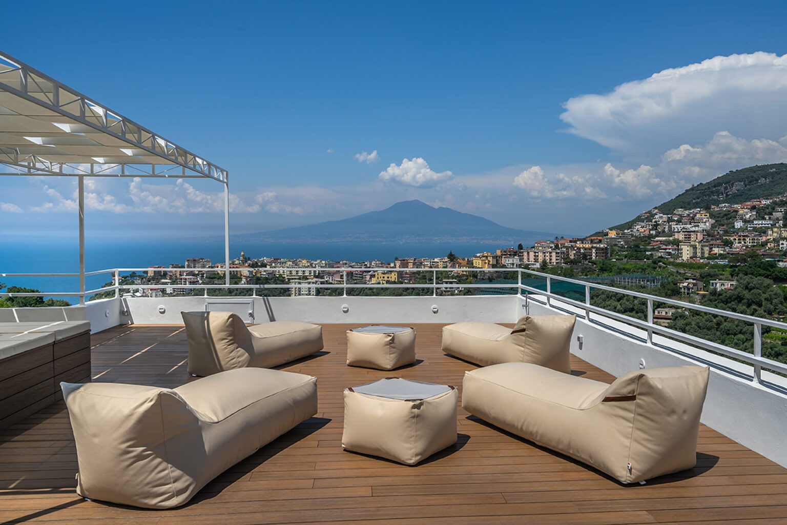 Rooftop terrace with modern bean bag seating overlooking a scenic view of the sea and mountains, featuring clear blue skies and distant cityscape. | Only on SopranoVillas