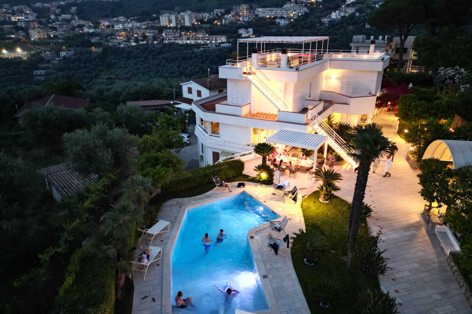 Luxurious villa with a swimming pool, surrounded by lush greenery and illuminated at night, offering a stunning view of the cityscape. | Only on SopranoVillas