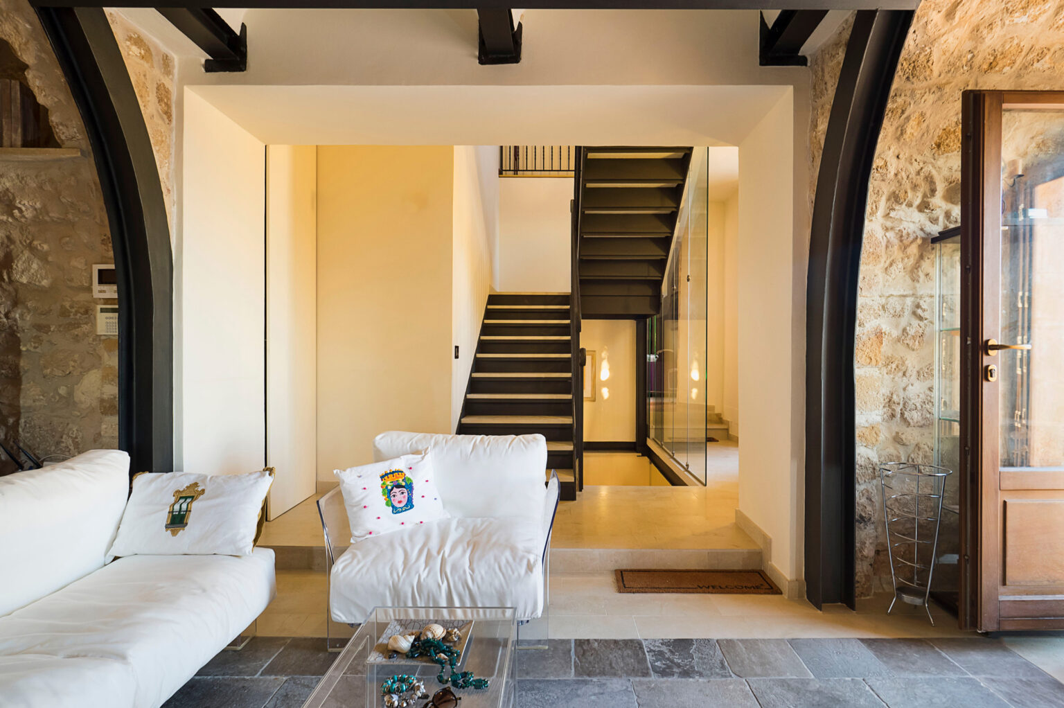 Modern living room with a white sofa, showcasing a stylish staircase in the background and natural stone walls, creating a warm and inviting atmosphere. | Only on SopranoVillas