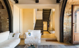 Modern living room with a white sofa, showcasing a stylish staircase in the background and natural stone walls, creating a warm and inviting atmosphere.