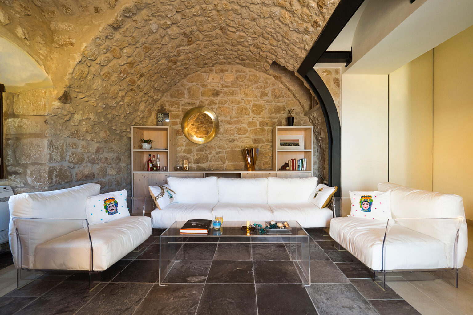 Stylish living room featuring a white sectional sofa, modern glass coffee table, and decorative shelves, set against a rustic stone archway backdrop. | Only on SopranoVillas