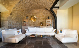 Stylish living room featuring a white sectional sofa, modern glass coffee table, and decorative shelves, set against a rustic stone archway backdrop.