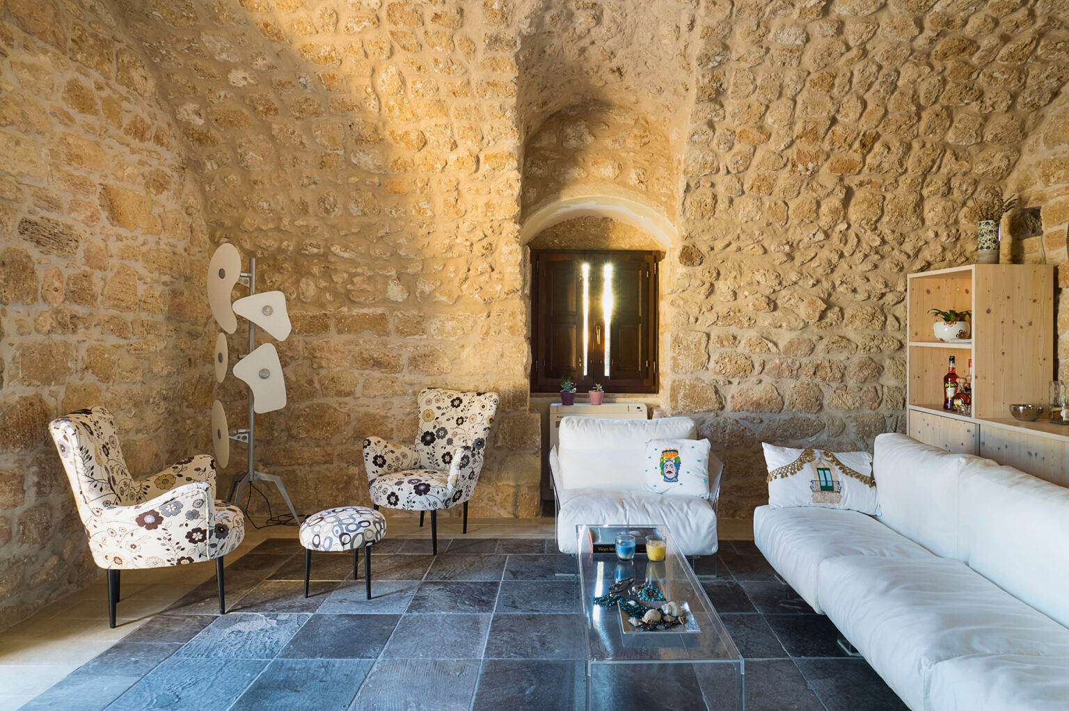 Cozy living room interior featuring stone walls, modern furniture, and a stylish design. The space includes a white sofa, patterned chairs, and a glass coffee table, enhancing the inviting atmosphere. | Only on SopranoVillas