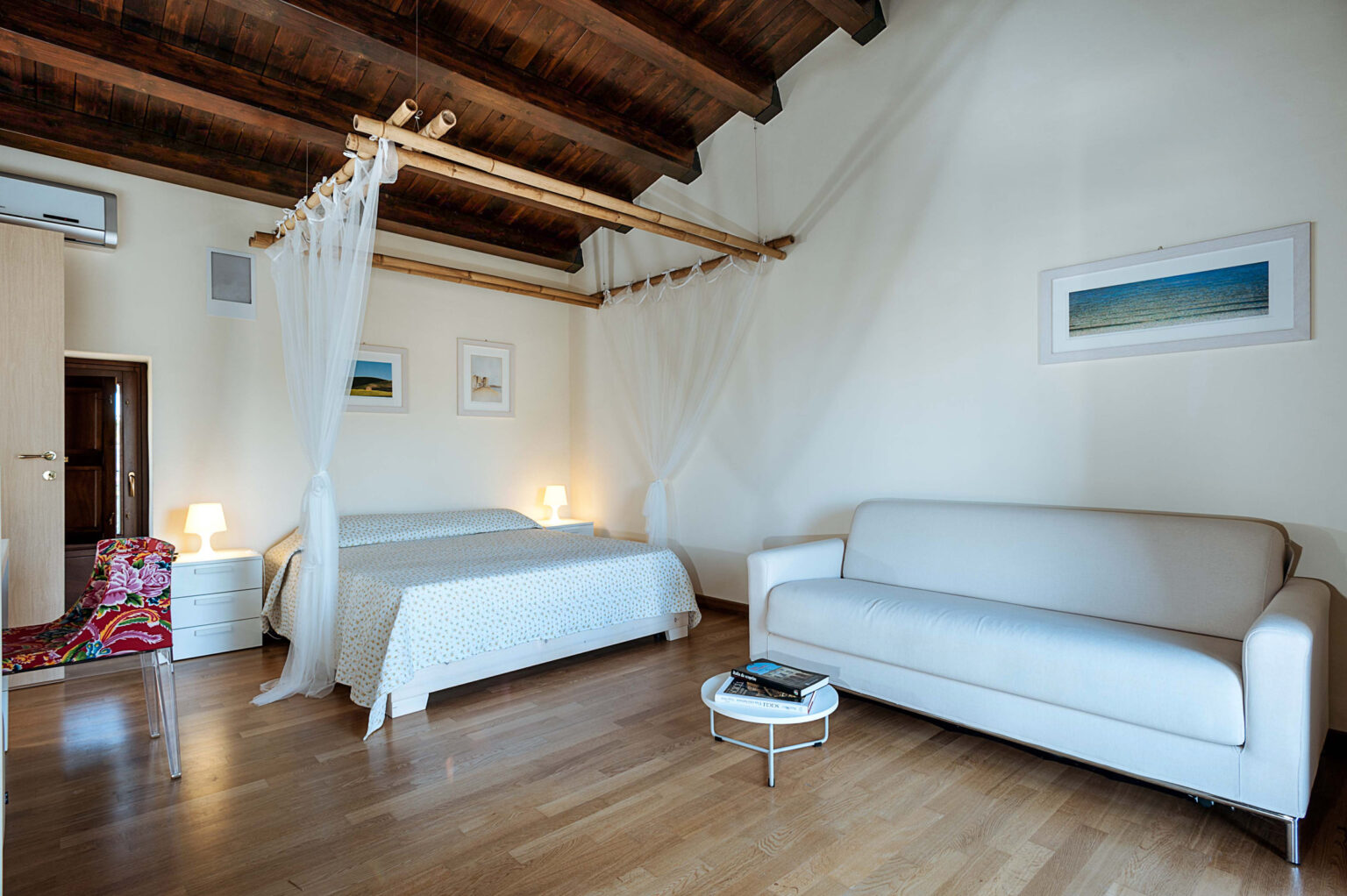 Cozy bedroom interior featuring a double bed with a canopy, a comfortable sofa, and warm wooden beams, complemented by soft lighting and minimalist decor. | Only on SopranoVillas