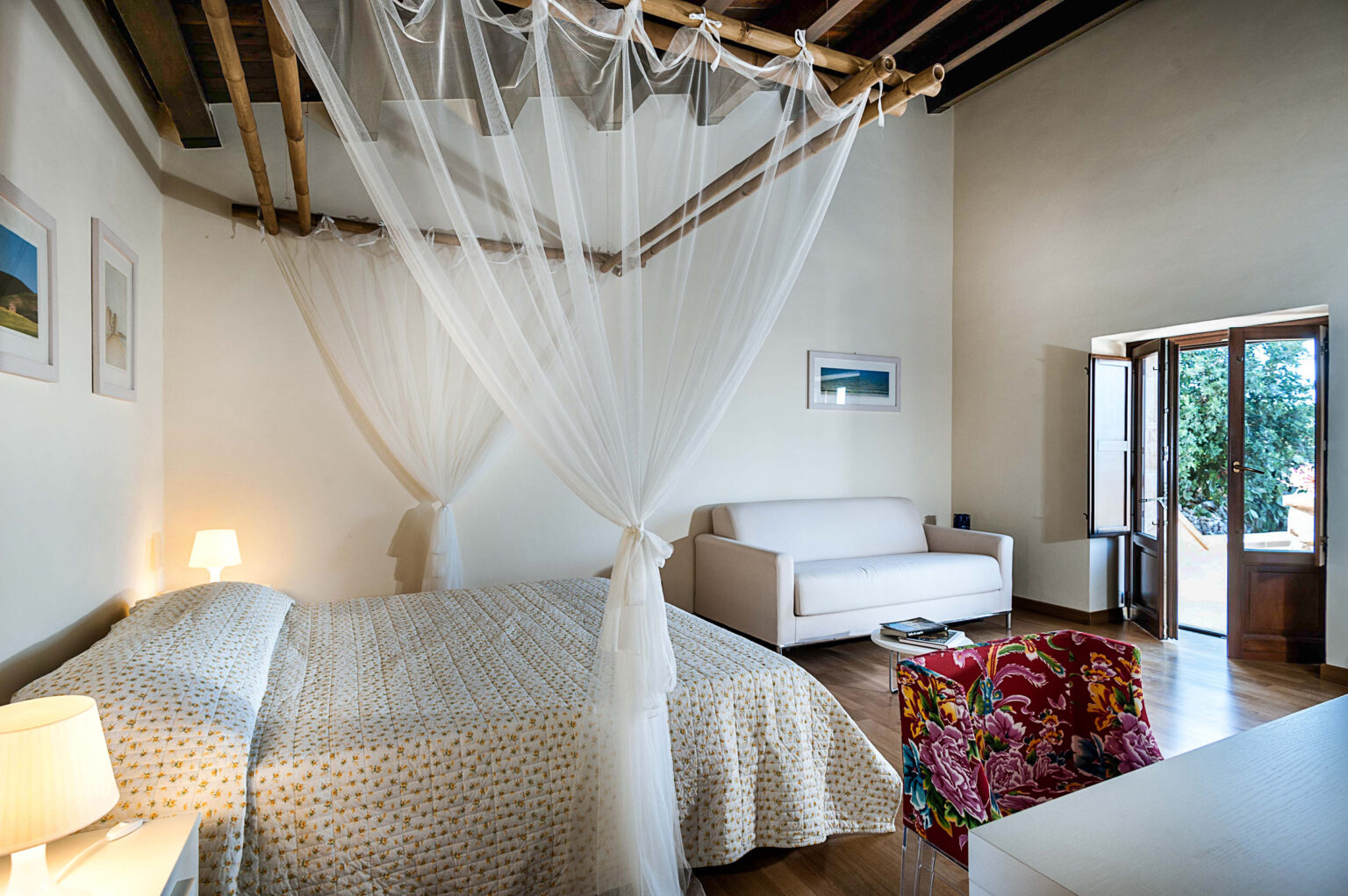 Cozy bedroom featuring a king-sized bed with a white canopy, a comfortable sofa, and large windows that allow natural light. Decor includes colorful accents and framed artwork, creating a warm and inviting atmosphere. | Only on SopranoVillas