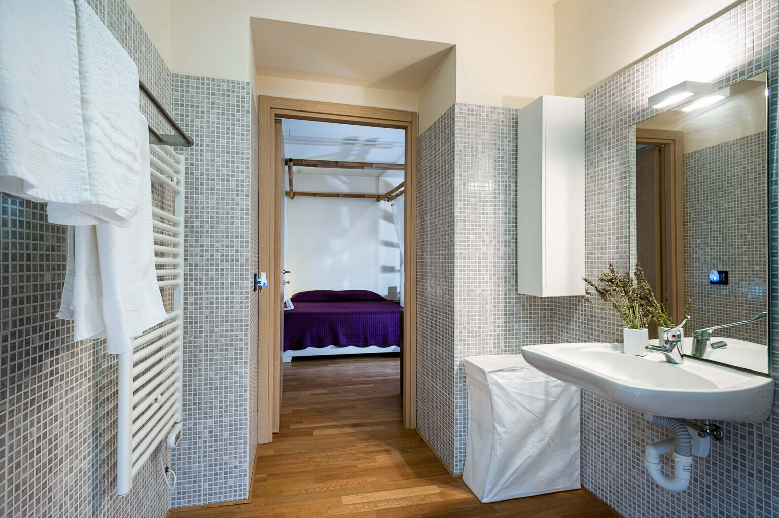 Modern bathroom interior featuring a sleek sink, towel rack, and mosaic tile walls, with a glimpse of a cozy bedroom in the background. | Only on SopranoVillas