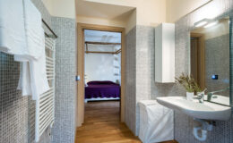 Modern bathroom interior featuring a sleek sink, towel rack, and mosaic tile walls, with a glimpse of a cozy bedroom in the background.
