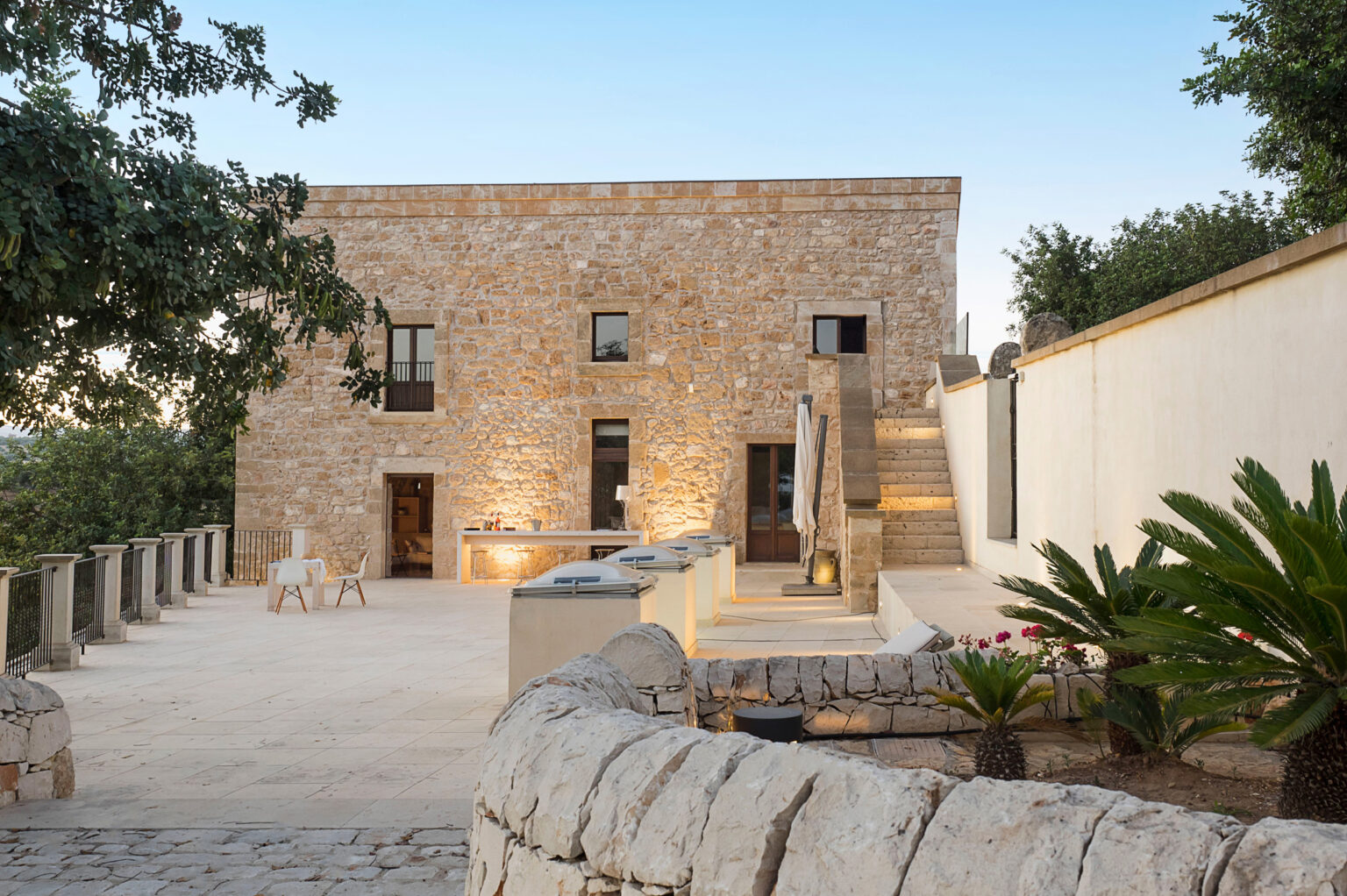 Exterior view of a modern stone villa with a spacious patio, featuring elegant outdoor seating and lush landscaping, highlighting a blend of contemporary and rustic architectural styles. | Only on SopranoVillas