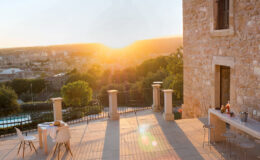 Scenic view of a stone terrace at sunset, featuring outdoor seating and a dining area with a beautiful landscape in the background. Ideal for relaxing or entertaining in a serene environment.