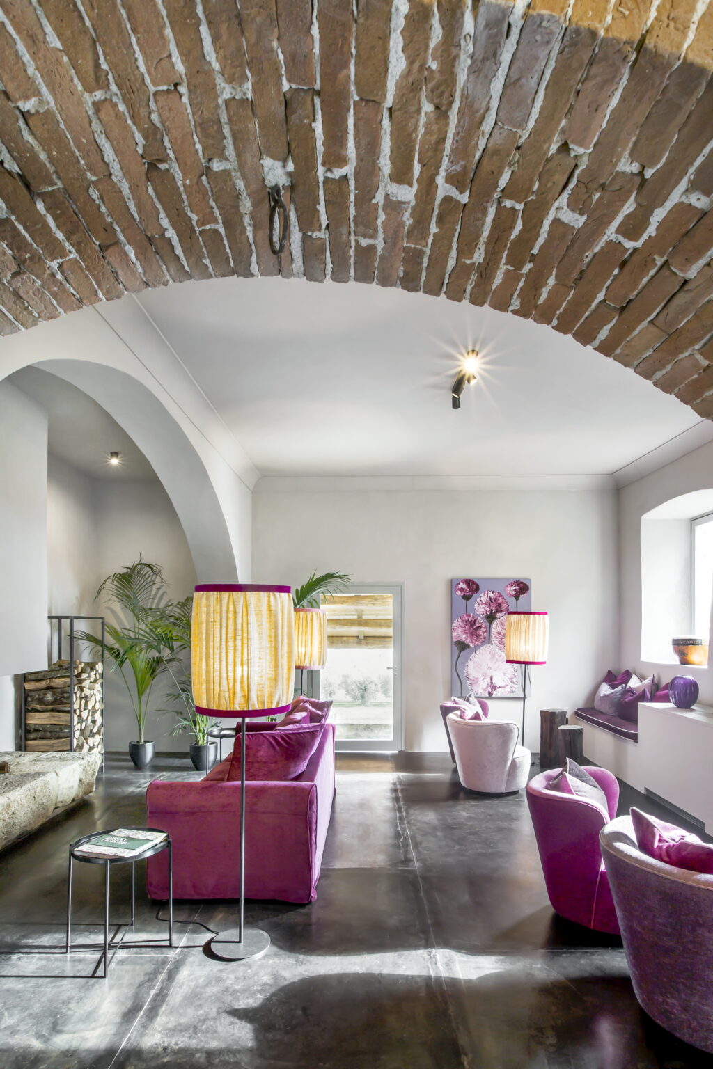 Modern interior design featuring elegant purple lamps, a stylish seating area, and artistic decor elements. The space is enhanced by natural light and unique architectural features like arched ceilings and exposed brick. | Only on SopranoVillas