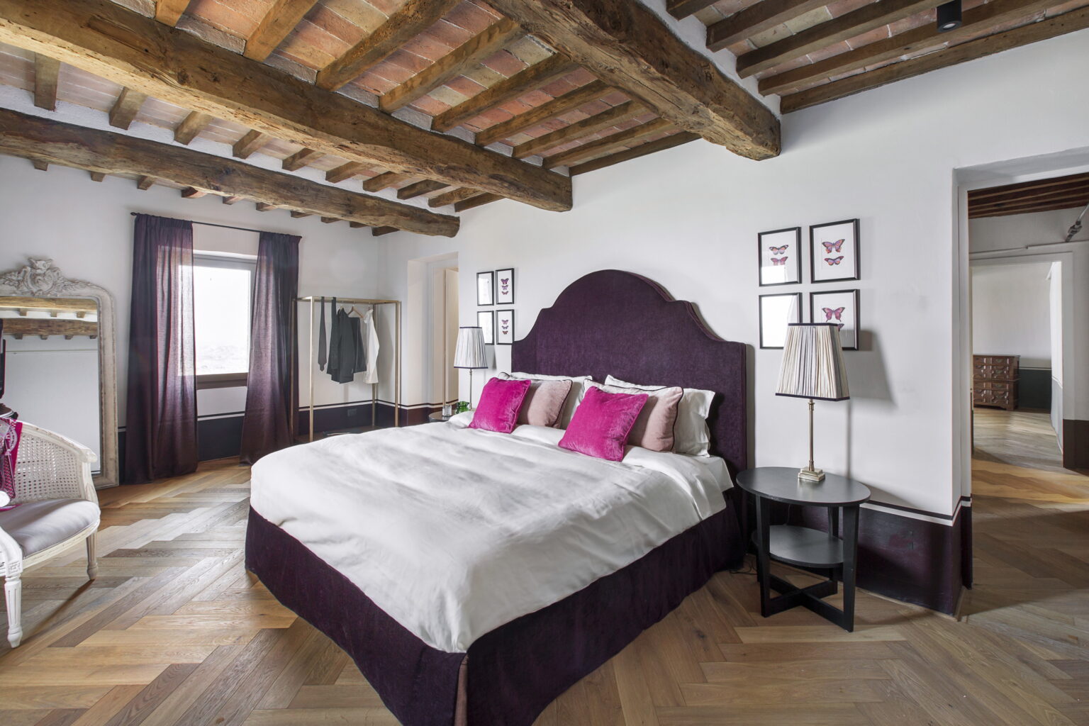Cozy bedroom featuring a plush bed with white linens and pink accent pillows, rustic wooden beams, elegant decor, and stylish furnishings, creating a warm and inviting atmosphere. | Only on SopranoVillas