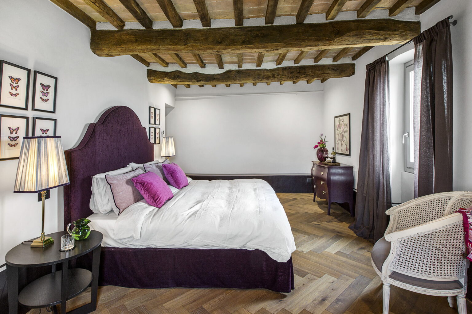 Cozy bedroom featuring a large bed with purple accents, wooden beam ceiling, and stylish decor, ideal for relaxation and comfort. The room includes elegant lighting and a tasteful arrangement of furniture, creating a warm atmosphere. | Only on SopranoVillas