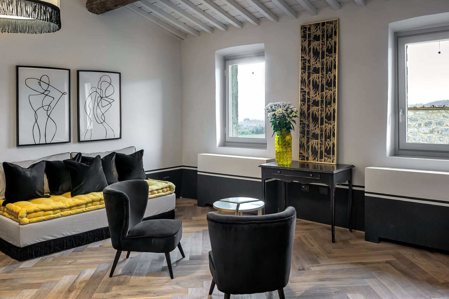 Modern living room featuring stylish black and yellow decor, two framed line art pieces on the wall, a sleek black chair, and a round coffee table. Natural light streams in through the windows, highlighting the elegant herringbone wooden floor. | Only on SopranoVillas