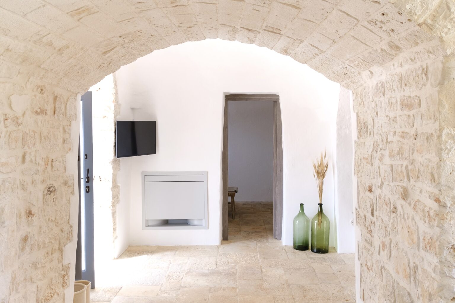 Interior view of a spacious, modern stone hallway featuring an arched ceiling, a wall-mounted television, and decorative green glass vases, creating a bright and inviting atmosphere. | Only on SopranoVillas