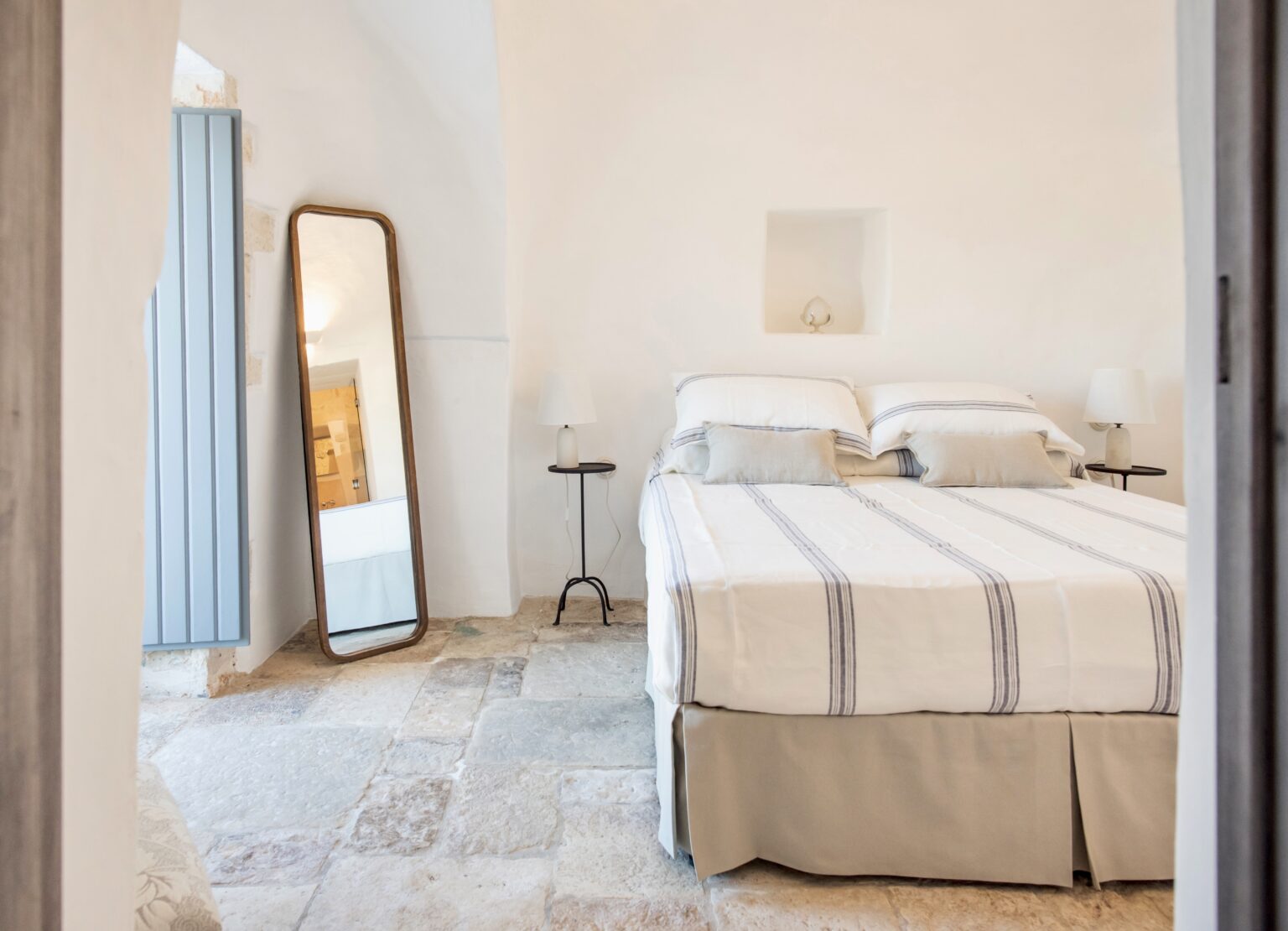 Cozy bedroom interior featuring a neatly made bed with striped bedding, a stylish mirror, and minimalist decor. The room has natural light and a serene atmosphere, ideal for relaxation. | Only on SopranoVillas