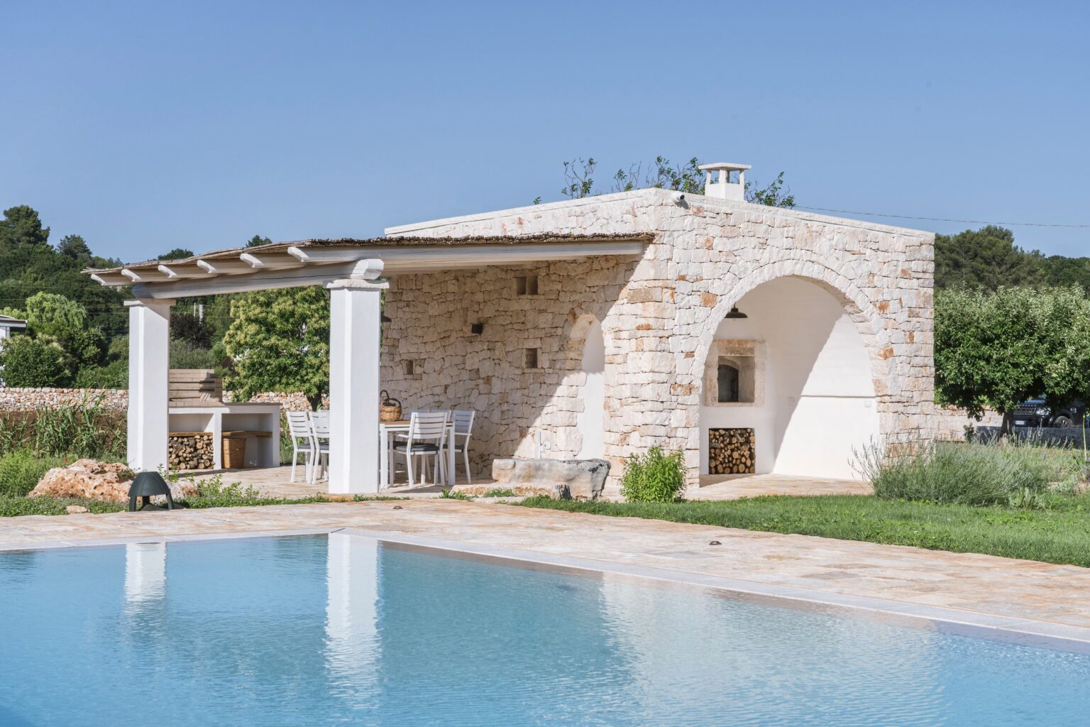 Modern stone villa with a swimming pool, featuring a shaded patio area and outdoor dining space surrounded by lush greenery. Ideal for relaxation and outdoor entertainment. | Only on SopranoVillas