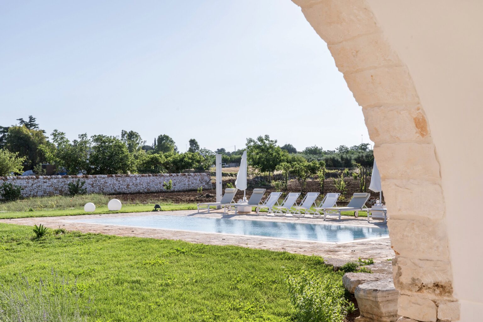 Serene outdoor pool surrounded by lush greenery and lounge chairs, framed by an elegant stone archway, perfect for relaxation in a tranquil setting. | Only on SopranoVillas