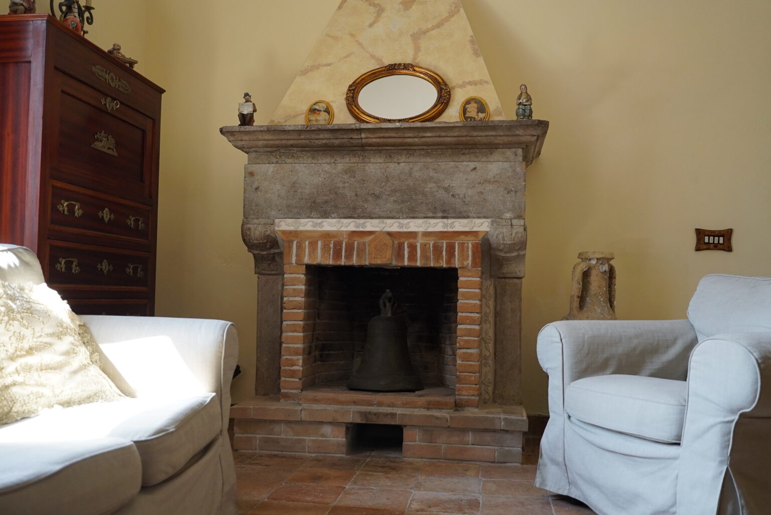 Cozy living room featuring a stone fireplace with a brick hearth, surrounded by light-colored armchairs and a wooden cabinet. Decorative items adorn the mantel, adding a warm and inviting atmosphere. | Only on SopranoVillas